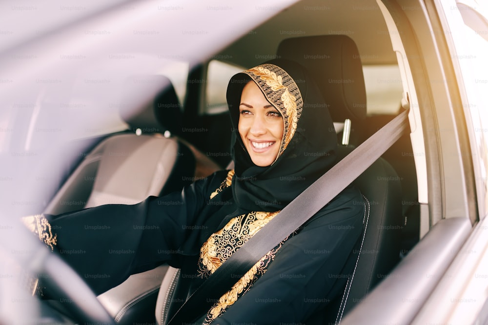 Beautiful muslim woman with toothy smile driving car.
