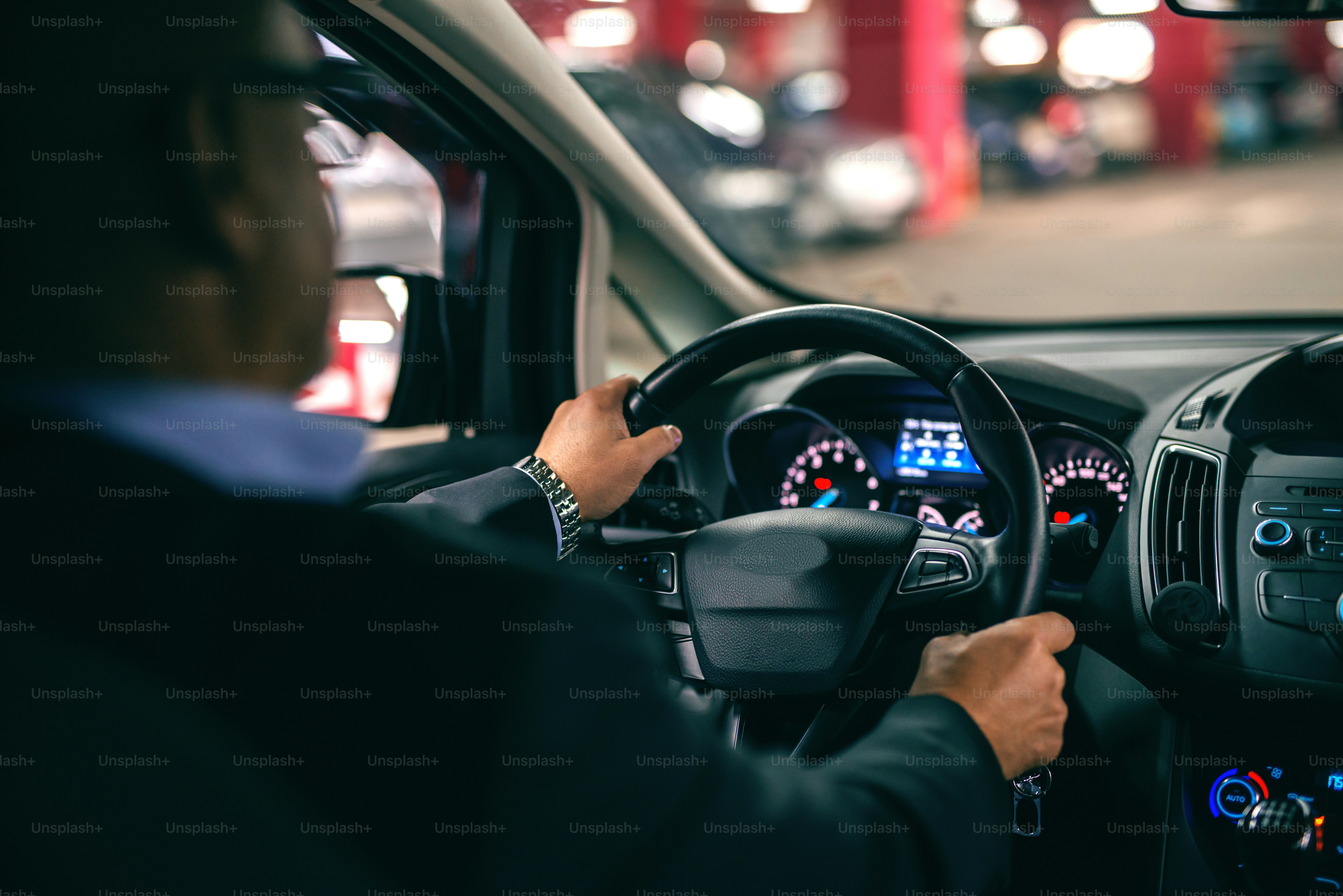 Man driving car at night, hands on wheel. Picture taken from backseat.