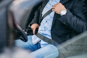 ひげを生やした年配の大人のビジネスマンが車のシートベルトを締める。