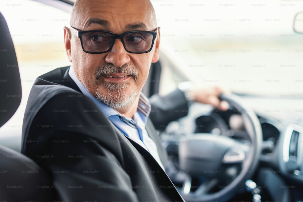 Bearded senior adult driving to reverse. Picture taken from the backseat.