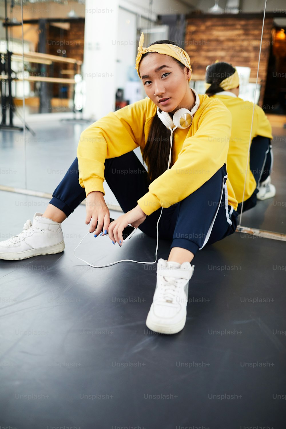 Jeune femme reposante en tenue de sport assise par terre dans un studio de danse moderne