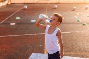 Garçon buvant de l’eau au biberon et debout sur le terrain après l’exercice.