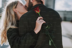 Close up of charming young lady holding red rose while sharing romantic moment with her boyfriend. Focus on woman hand with flower