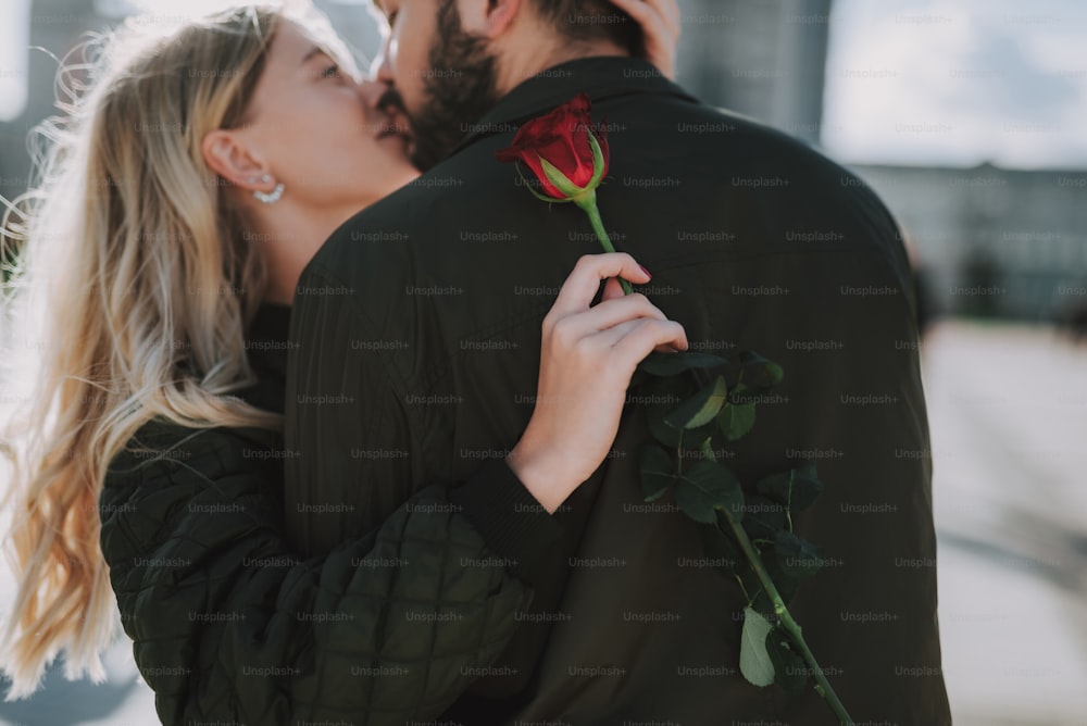 Gros plan d’une charmante jeune femme tenant une rose rouge tout en partageant un moment romantique avec son petit ami. Focus sur la main de la femme avec la fleur