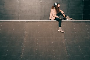Adolescente hipster mestiça com expressão facial séria apreciando música e sentada no skate park.