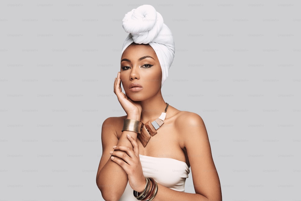 Attractive young African woman in turban looking at camera while standing against grey background