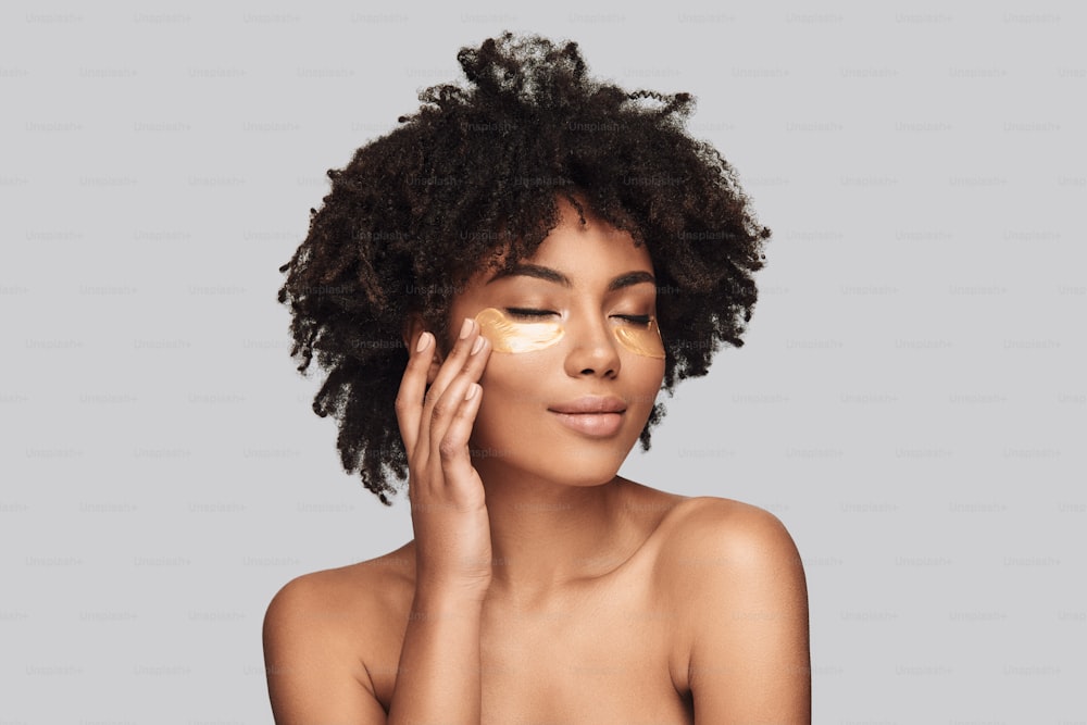 Attractive young African woman applying medical eye patch and smiling while standing against grey background