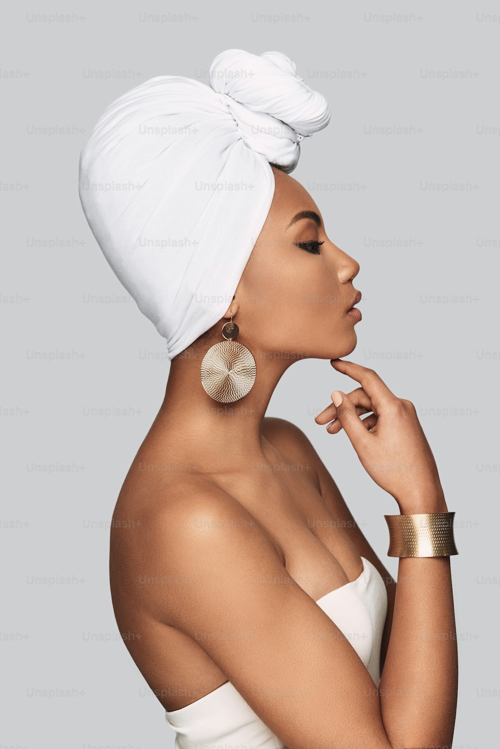 Side view of attractive young African woman in turban keeping hand on chin while standing against grey background