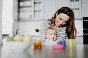 Smiling woman holding her child in arms and admiring him. He is keeping his fingers in mouth. Happy motherhood concept