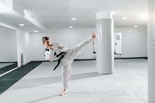 Menino caucasiano em dobok chutando em pose dollyo-chagi. Conceito de treinamento de Taekwondo.