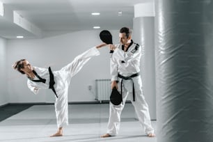 Chica discapacitada caucásica altamente motivada que practica taekwondo con su entrenamiento. Chica pateando patada objetivo.