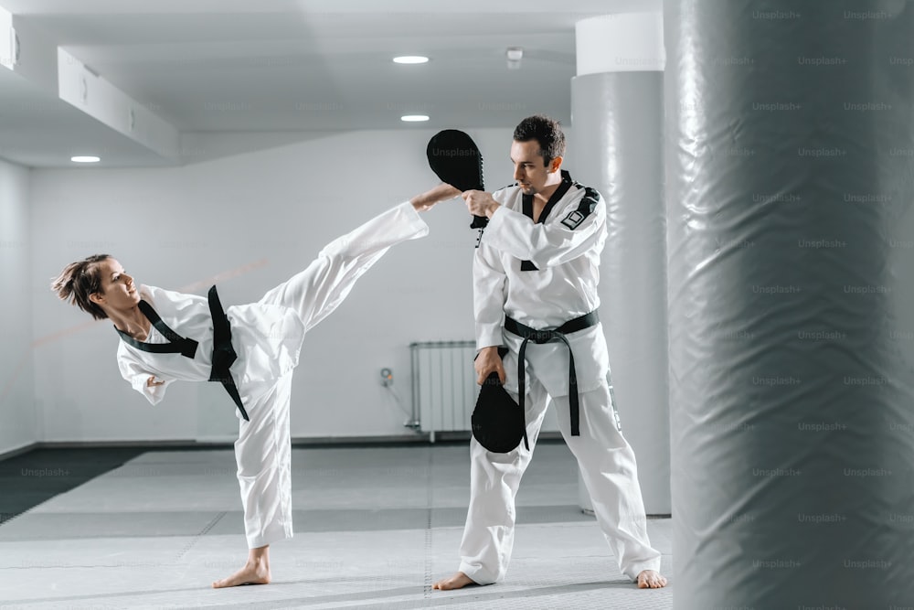 Fille handicapée caucasienne très motivée pratiquant le taekwondo avec son entraînement. Fille donnant un coup de pied à la cible.