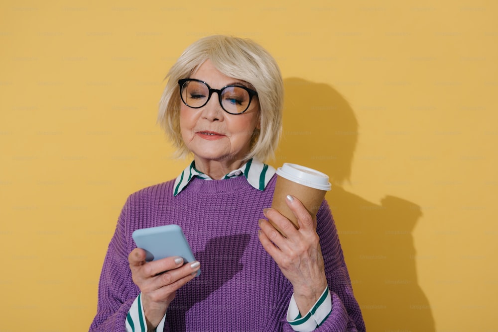 Half length of Caucasian old lady looking at screen of mobile phone and typing a message. She is wearing eyeglasses while posing in studio