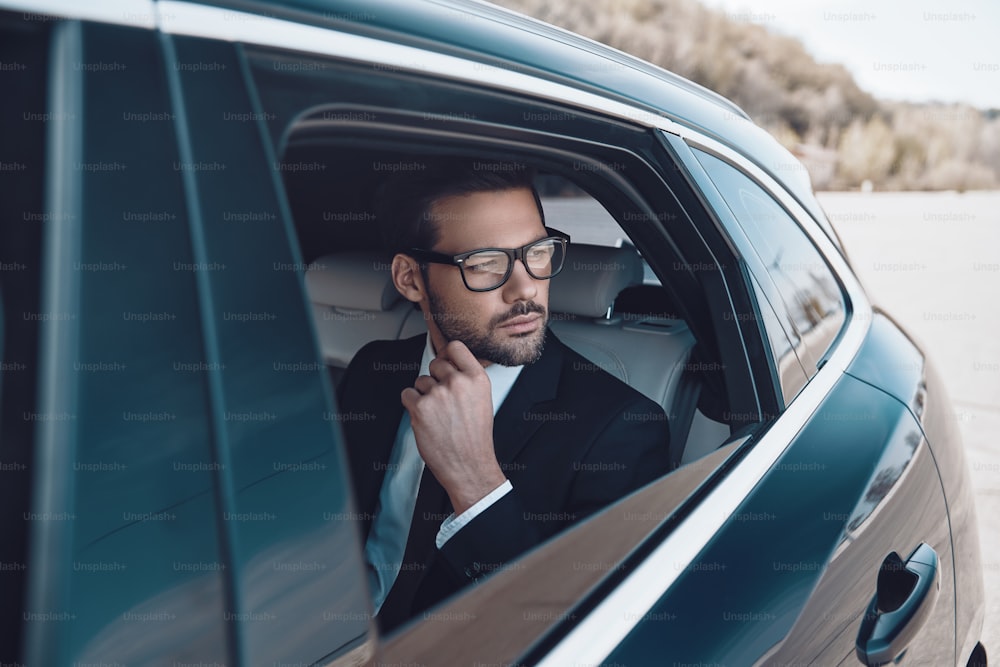 Nachdenklicher junger Geschäftsmann, der die Hand am Kinn hält, während er im Auto sitzt
