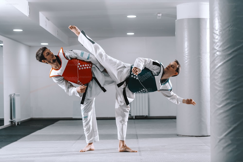 Two Caucasian sporty men sparring in tekwondo fittings barefoot.