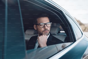 Joven empresario reflexivo manteniendo la mano en la barbilla mientras está sentado en el auto