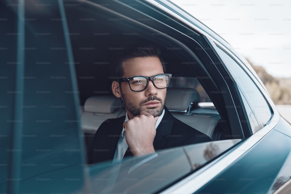 Thoughtful young businessman keeping hand on chin while sitting in the car