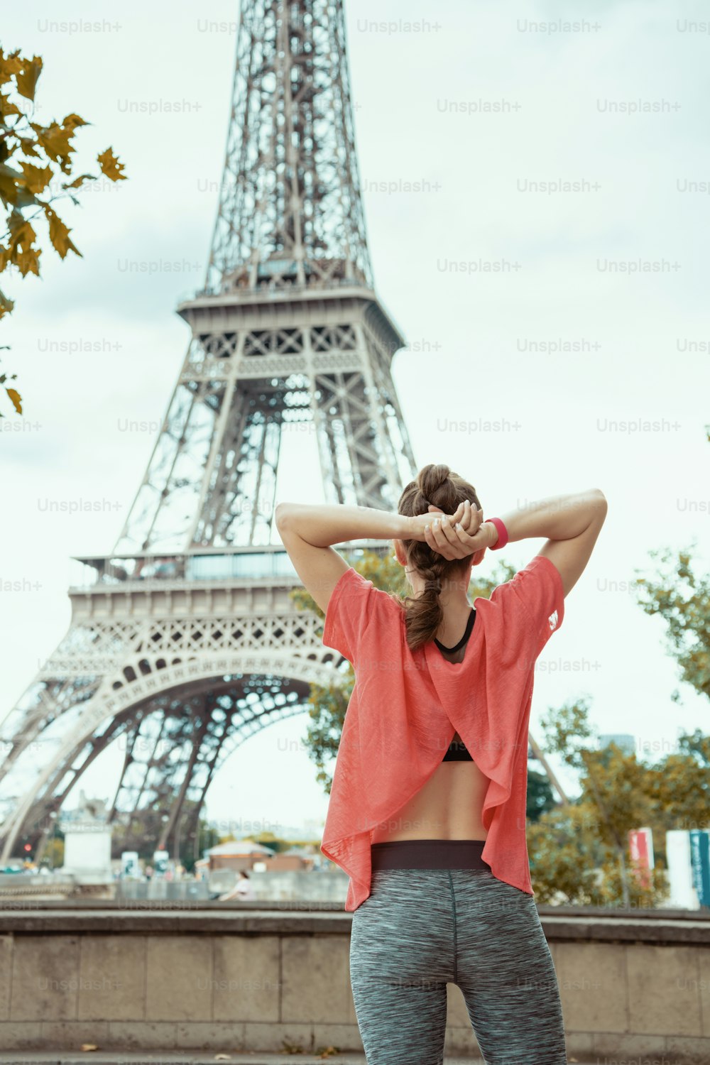 Seen from behind young woman jogger in sport clothes in the front of Eiffel tower in Paris, France.