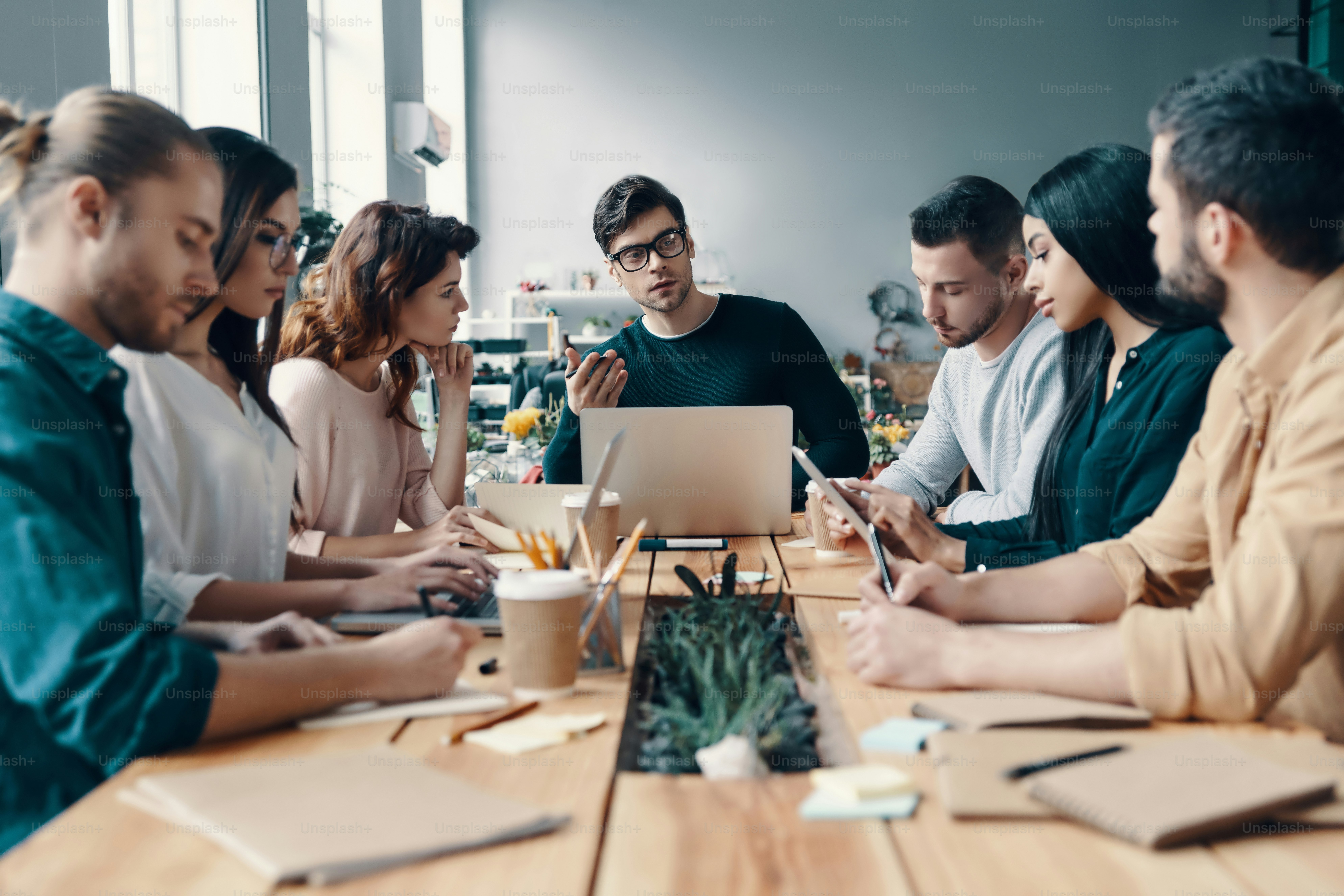 Group of young modern people in smart casual wear discussing something while working in the creative office