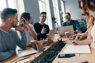 Group of young modern people in smart casual wear discussing something and smiling while working in the creative office