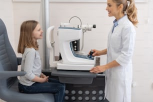 Vista laterale ritratto di oculista amichevole che utilizza il rifrattometro automatico durante l'esame degli occhi del bambino. Si guardano e sorridono