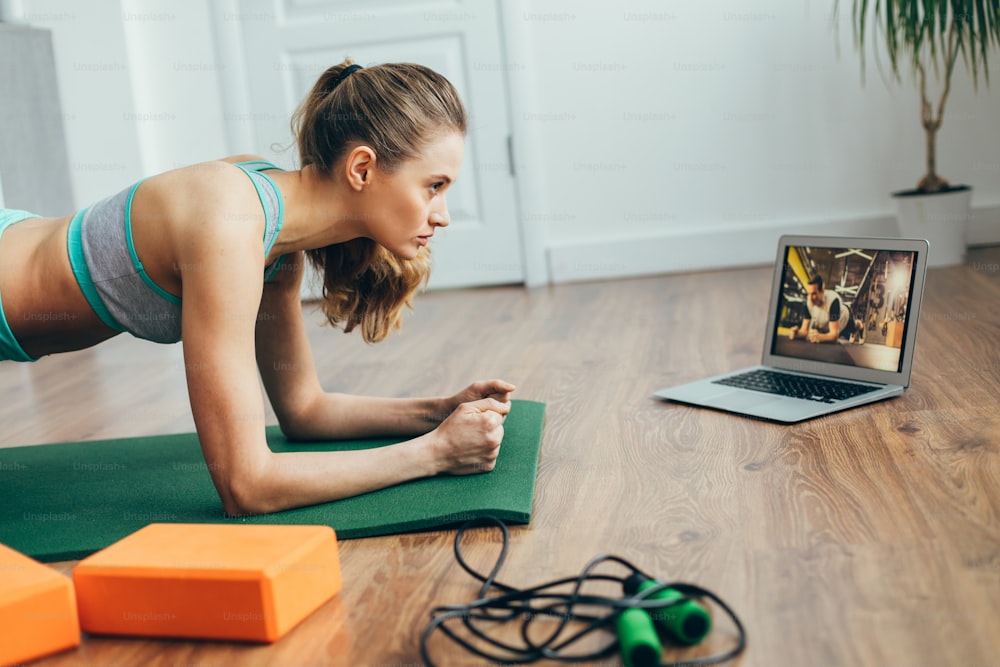 Health practice concept. Waist up side on portrait of young woman in sportswear doing plank exercise on mat at home