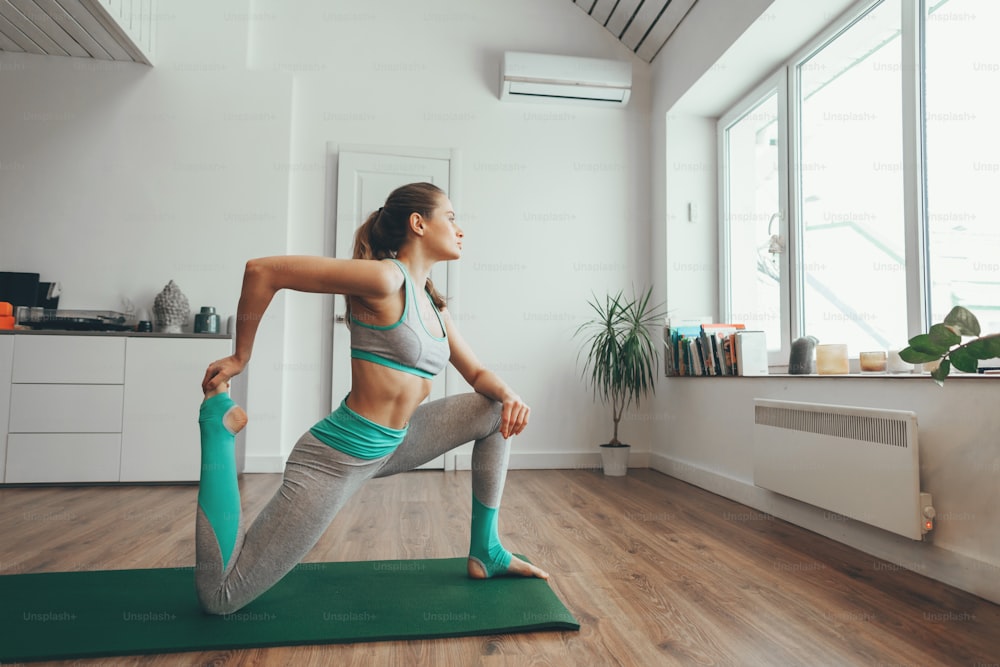 Concepto de práctica de salud y estiramiento. Lado en el retrato de una joven equilibrada haciendo una pose de yoga en una colchoneta en casa