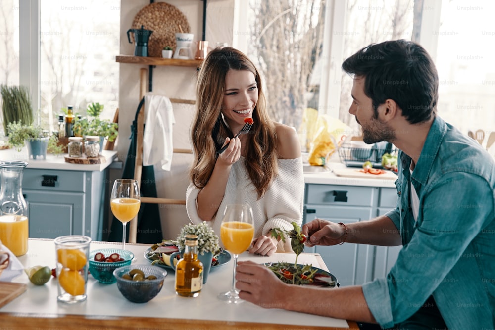 Beautiful young couple enjoying healthy breakfast while sitting in the kitchen at home