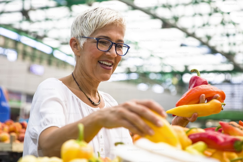 Portrait of good-looking senior woman wearing glasses buys pepper on market