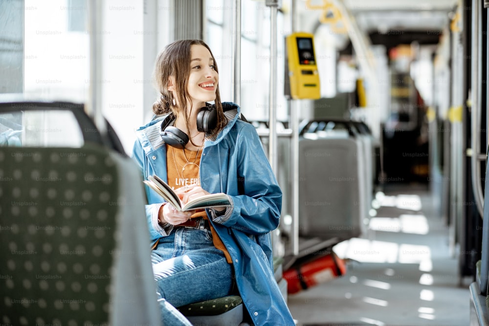 Junge Frau, die Buch liest, während sie sich in der modernen Straßenbahn bewegt, glückliche Fahrgastin in den öffentlichen Verkehrsmitteln