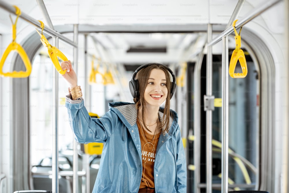 Junge Frau hält Griff, während sie sich in der modernen Straßenbahn bewegt. Glücklicher Passagier, der die Fahrt mit den öffentlichen Verkehrsmitteln genießt
