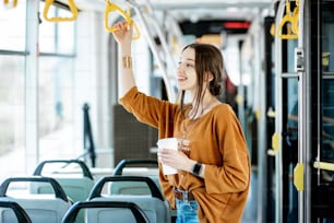 젊고 행복한 승객은 현대 트램에서 커피와 함께 서서 대중 교통에서 여행을 즐기고 있습니다