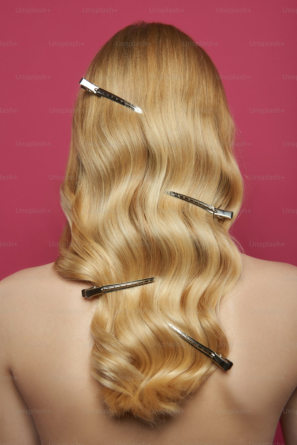 Beauty and hairstyle. Close up back side portrait of young graceful naked blonde woman with barrette alligator clips in wavy locks. Isolated on pink