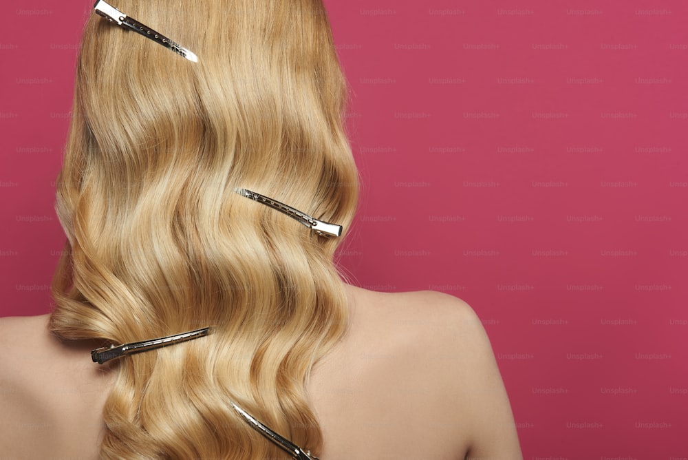 Beauty and hairstyle. Close up portrait of young naked blonde lady with barrette alligator clips in wavy locks. Isolated on pink with copy space on right