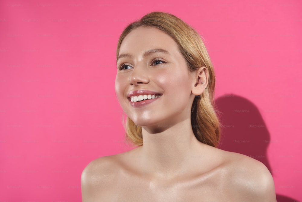 Concepto de belleza natural. Retrato en primer plano de una mujer rubia sonriente y feliz en topless con maquillaje desnudo que permanece aislada en rosa