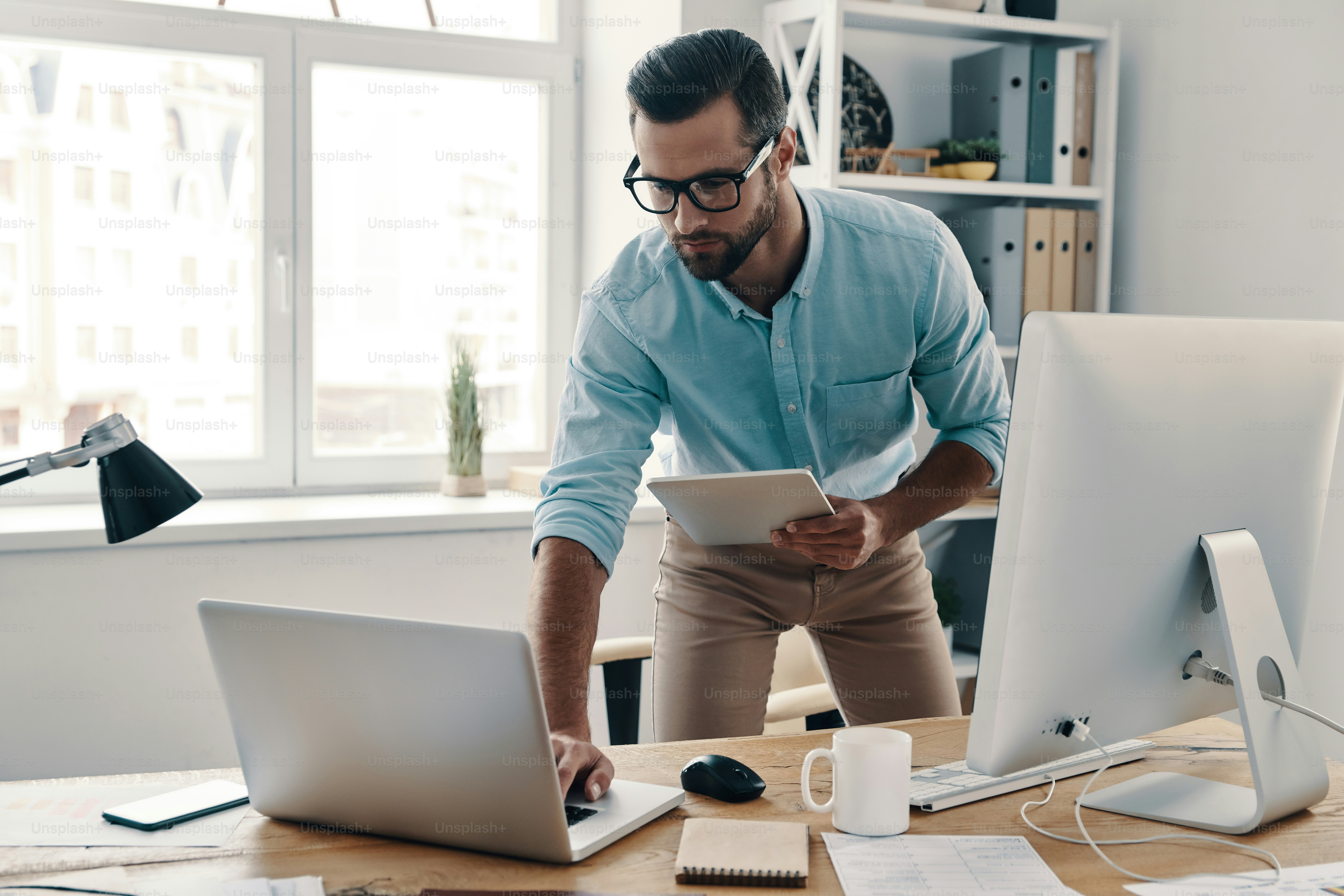 Young modern businessman using digital tablet and laptop while working in the office