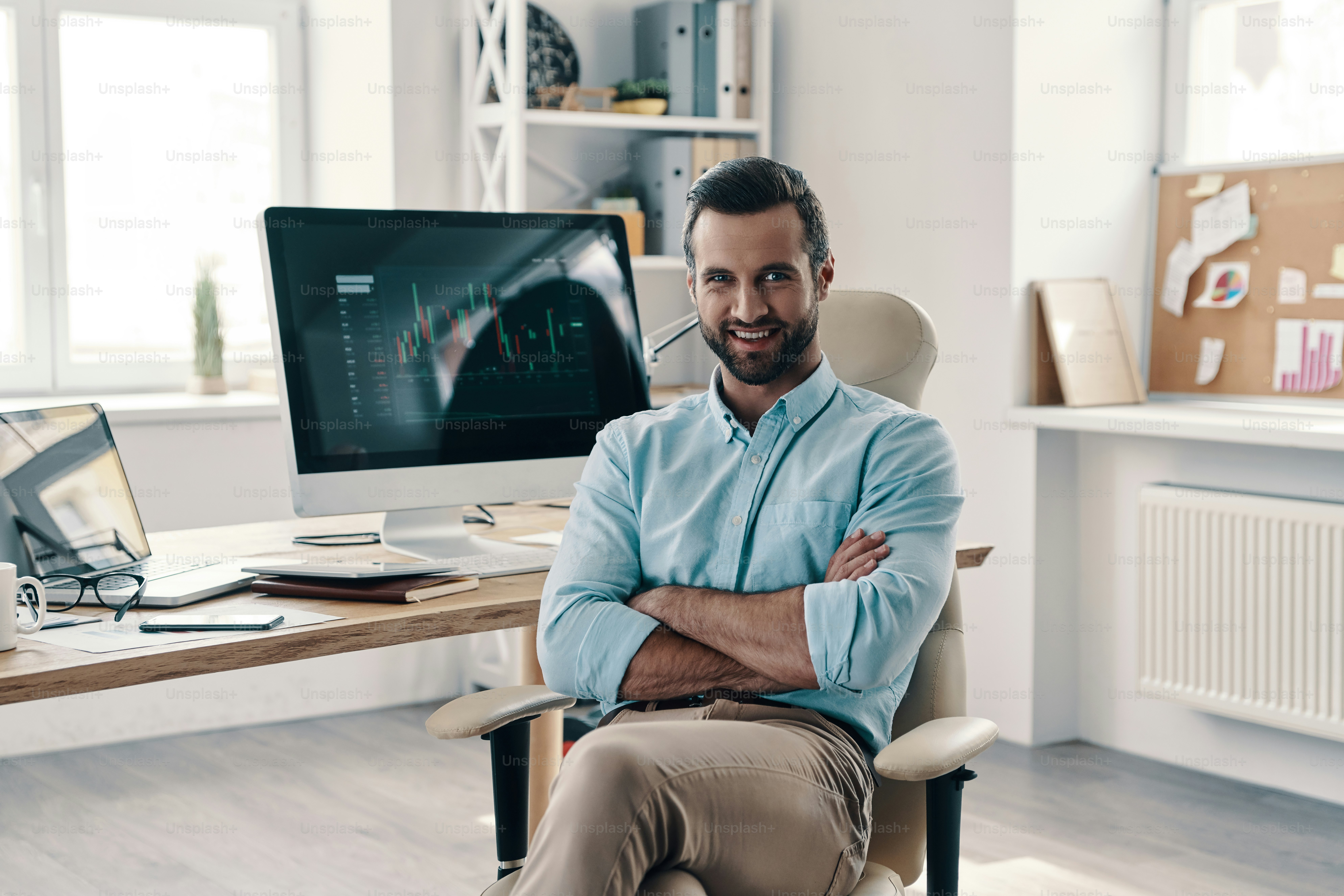 Young modern businessman looking at camera and smiling while sitting in the office