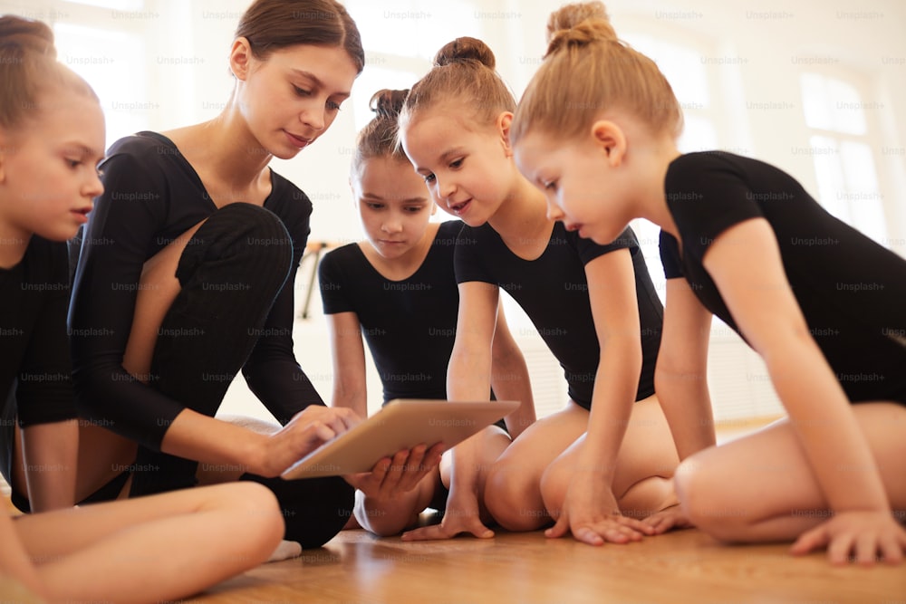 Retrato de una maestra con un grupo de niñas viendo videos a través de una tableta digital durante la práctica de baile en el estudio