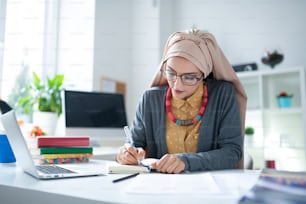 Table with books. Busy Muslim teacher wearing hijab sitting at the table with books and working