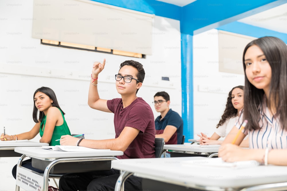 Confident student with raised hand attending lecture in classroom at school
