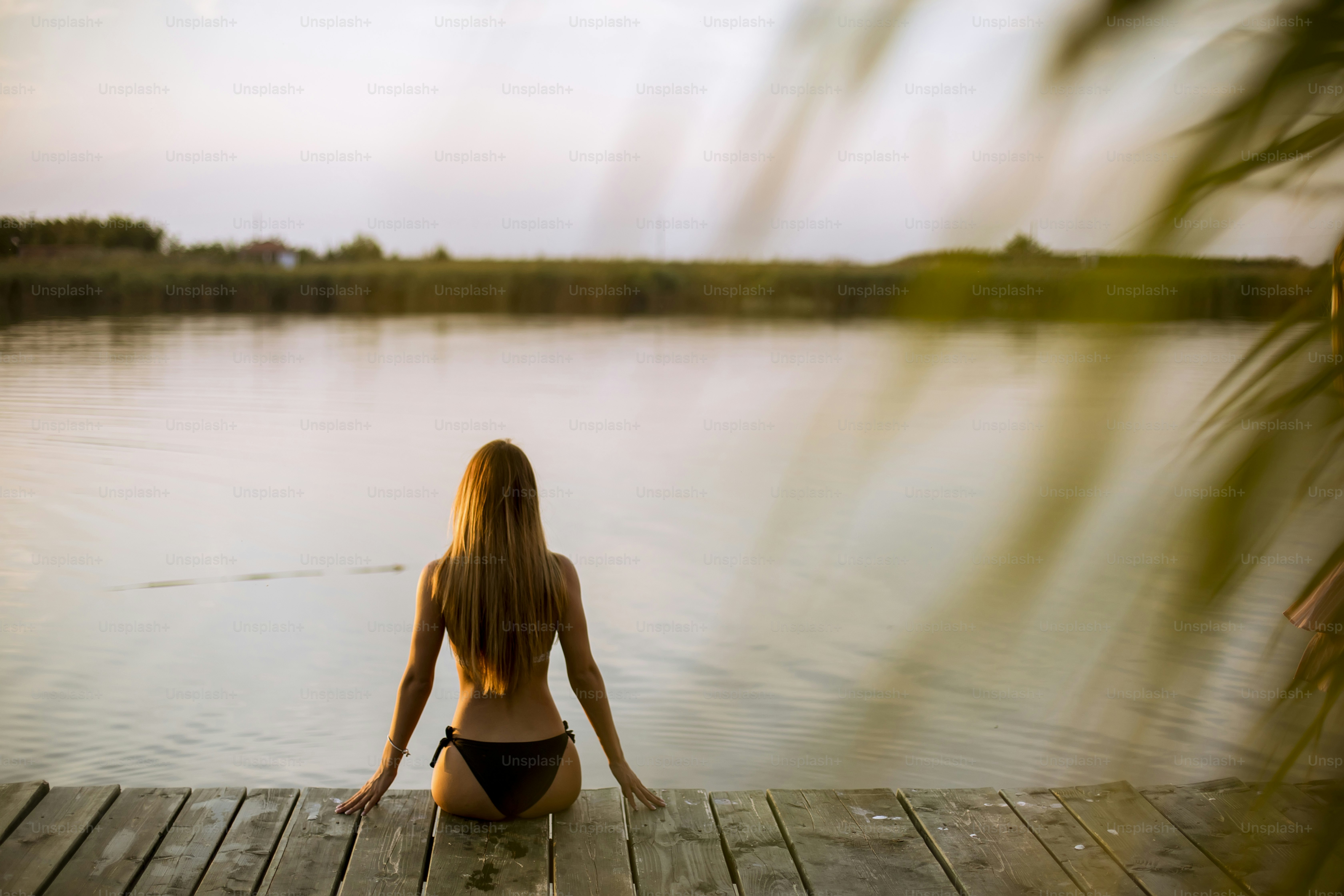 A young woman sitting on a wooden dock beside a calm lake, her phone turned off beside her, as the sun rises over the horizon.