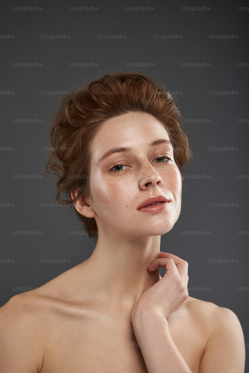 Ritratto ravvicinato di giovane donna attraente con taglio di capelli elegante che guarda la fotocamera e tiene le labbra leggermente divaricate. Isolato su sfondo grigio