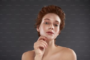 Retrato en primer plano de una atractiva joven con un elegante corte de pelo mirando a la cámara y manteniendo los labios ligeramente separados. Aislado sobre fondo gris