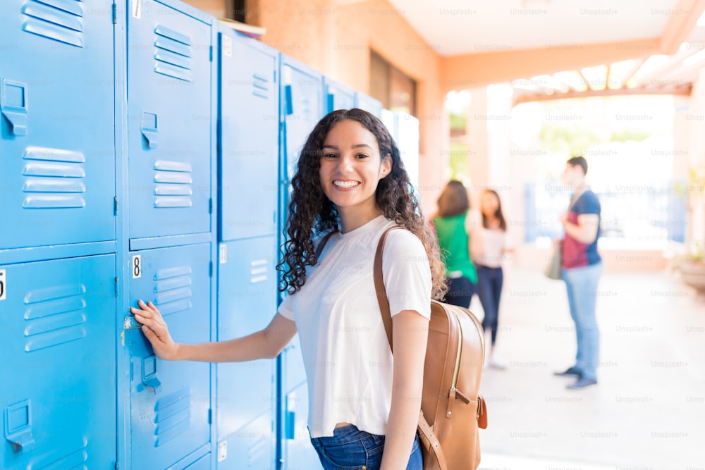 Portrait of smiling teenager standing by lockers in university