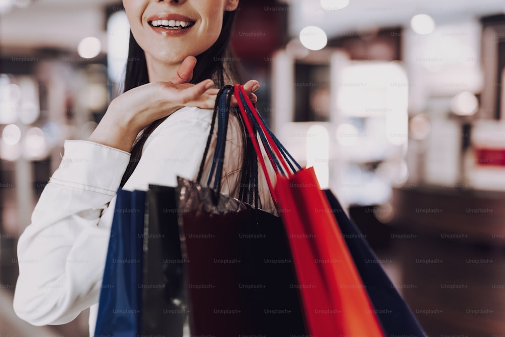 Concéntrese en el primer plano de la sonrisa femenina mientras sostiene bolsas de papel con las compras. Ella está pasando tiempo en un centro comercial