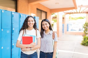 Happy female high school girls standing near lockers in corridor