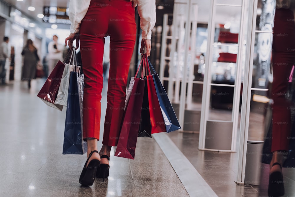 Concentrati sulla donna magra che indossa i tacchi che cammina vicino alle boutique. Sta trasportando sacchetti di carta con acquisti. Copia lo spazio sul lato destro