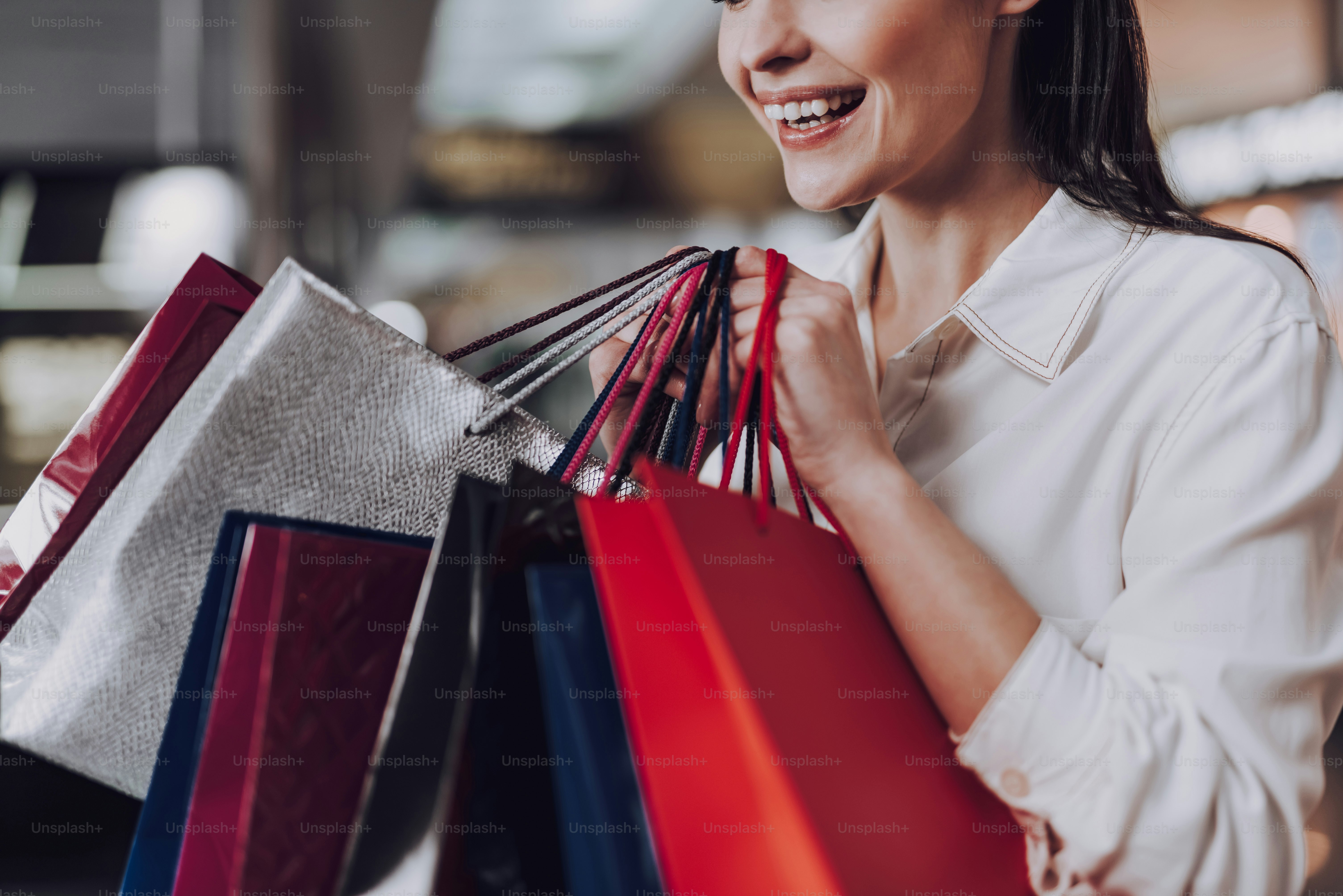 Focus on close-up of laughing female standing inside airport. She is holding paper packets with purchases
