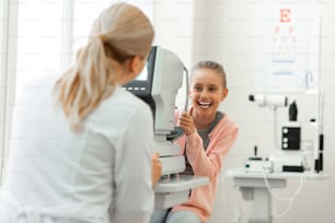 Important appointment. Laughing pretty girl with tied hair having fun while visiting medical cabinet and checking vision