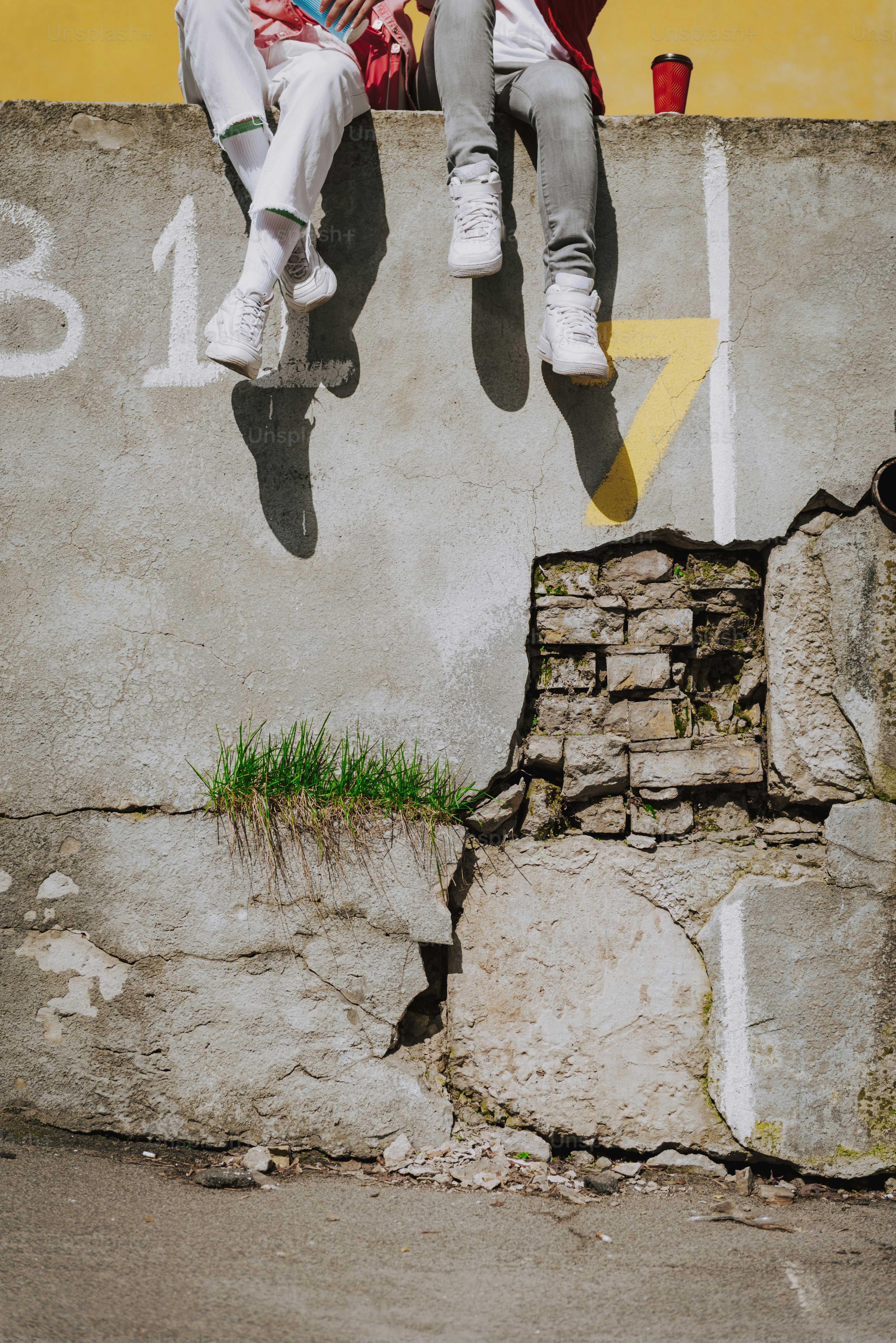Urban lifestyle concept. Waist down portrait of two hipster ladies in sporty stylish clothes resting together on old parapet with coffee